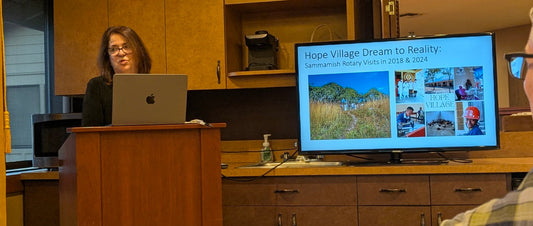 A speaker presents to Sammamish Rotary beside a screen showing Hope Village’s development between 2018 and 2024.